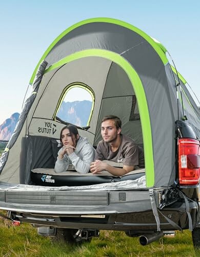 Two people relaxing inside a tent set up in a truck bed.